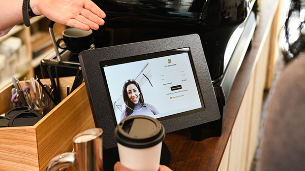 L'image 6 présente la technologie de reconnaissance faciale des caisses de Mastercard, illustrée par une tablette sur laquelle figure le visage d'une femme. Un cercle blanc autour de son visage montre la capacité de reconnaissance faciale de la technologie.